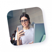 Portrait d’une jeune femme portant des lunettes, souriante, travaillant sur ordinateur et consultant son téléphone, illustrant la modernité et la réactivité des agents actifs de Naya.