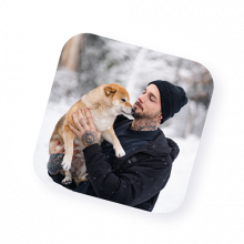 Portrait d’un homme en manteau noir et bonnet jouant avec un chien dans la neige, illustrant la complicité et la diversité des agents actifs de Naya.