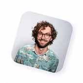 Portrait d’un homme souriant, cheveux bouclés et lunettes, sur fond clair, incarnant la diversité et l’accessibilité des agents actifs de Naya.