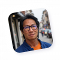 Portrait d’un homme souriant aux cheveux noirs et lunettes bleues, photographié en extérieur urbain, illustrant la diversité des agents actifs de Naya.