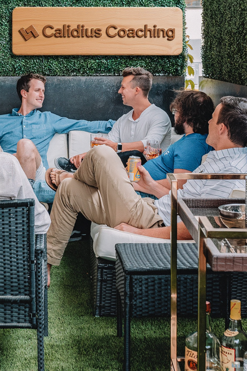 Petit groupe de personnes discutant de façon informelle dans un espace extérieur cosy, sous une enseigne “Calidius Coaching”, illustrant la convivialité et l’esprit d’équipe.