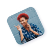 Portrait d’une jeune femme aux cheveux rouges, souriante et faisant un geste complice de la main, posée devant un mur bleu.