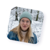 Portrait d’une jeune femme blonde portant des lunettes et un bonnet, souriant dans une forêt enneigée, illustrant la diversité et la chaleur humaine des agents actifs de Naya.